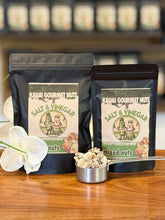 Two packages of Kauai Gourmet Nuts Salt & Vinegar mixed nuts on a wooden surface with a white flower.