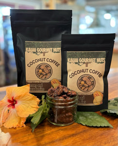 Two packages of Kauai Gourmet Nuts Coconut Coffee on a wooden surface with a flower and jar of coffee beans.