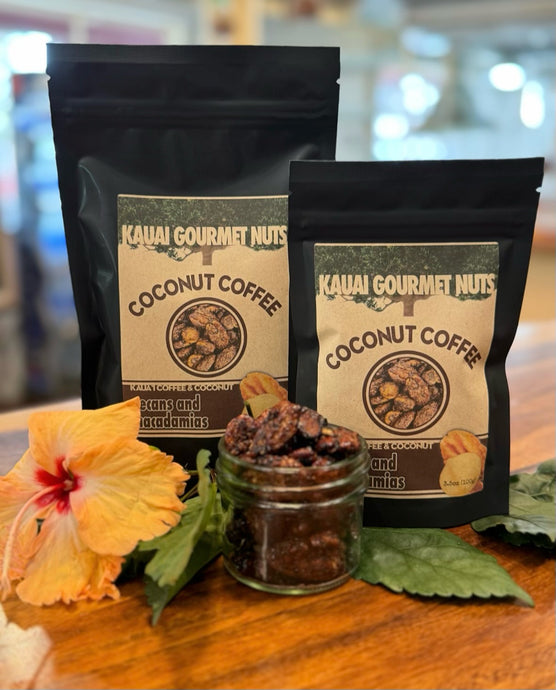 Two packages of Kauai Gourmet Nuts Coconut Coffee on a wooden surface with a flower and jar of coffee beans.